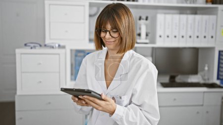 Photo for Smiling young latina, a beautiful lab scientist at work. harnessing the power of tech touchpad while mastering medical research indoors! - Royalty Free Image