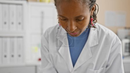 Foto de Mujer afroamericana con bata blanca de laboratorio enfocada en el trabajo en un entorno de laboratorio médico. - Imagen libre de derechos