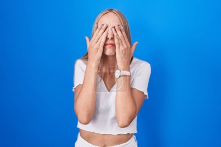 Photo for Young caucasian woman standing over blue background rubbing eyes for fatigue and headache, sleepy and tired expression. vision problem - Royalty Free Image