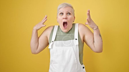 Photo for Middle age grey-haired woman standing with surprise expression over isolated yellow background - Royalty Free Image