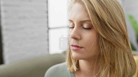 Foto de Caucásica, mujer adulta con el pelo corto y rubio, sentada en un sofá en una serena sala de estar. - Imagen libre de derechos