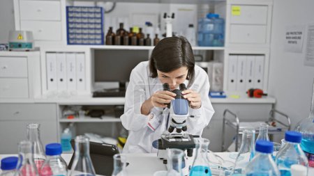 Téléchargez les photos : Jeune femme hispanique jeune scientifique utilisant le microscope au laboratoire - en image libre de droit