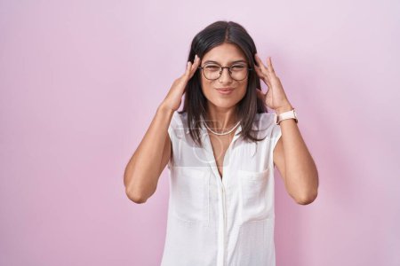 Téléchargez les photos : Brunette jeune femme debout sur fond rose portant des lunettes avec la main sur la tête, maux de tête parce que le stress. migraine souffrant. - en image libre de droit
