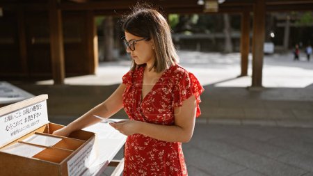 Photo for Beautiful hispanic woman with glasses makes a lunar wish at meiji temple, embracing japanese culture and tradition - Royalty Free Image