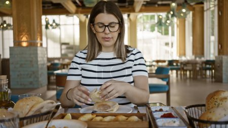Foto de Una joven morena adulta disfruta de una comida sola en un restaurante moderno, ejemplificando una experiencia culinaria casual. - Imagen libre de derechos
