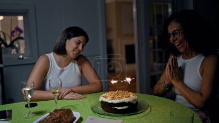 Photo for Two women celebrating with sparklers on a carrot cake in a cozy home interior, expressing joy and togetherness. - Royalty Free Image