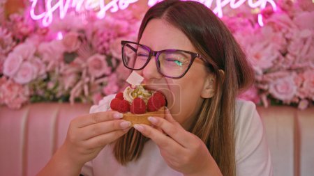 Téléchargez les photos : Une jeune femme profite d'une tarte dans un café à thème rose orné de fleurs et de néons. - en image libre de droit