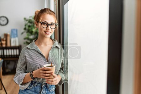 Téléchargez les photos : Jeune femme caucasienne travailleur d'affaires souriant confiance boire du café au bureau - en image libre de droit