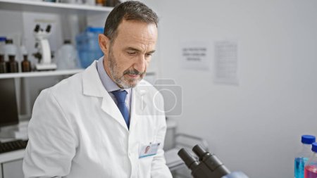 Photo for Aged man with grey hair, a scientist busy in his lab, peering into microscope for medical discovery - Royalty Free Image