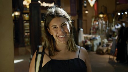 Téléchargez les photos : Une jeune femme brune souriante explore le souk traditionnel de dubai, incarnant un mélange de culture et de modernité. - en image libre de droit