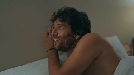 Photo for Young hispanic man listening through wall with glass lying on bed shirtless at bedroom - Royalty Free Image