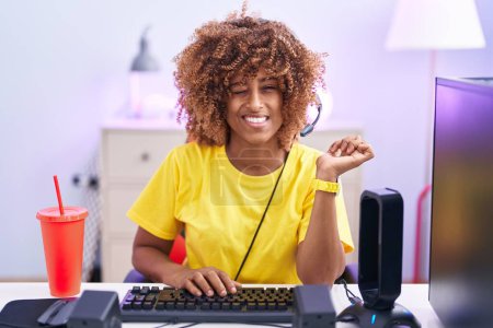 Photo for Young hispanic woman with curly hair playing video games wearing headphones winking looking at the camera with sexy expression, cheerful and happy face. - Royalty Free Image