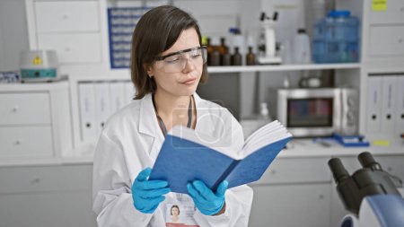 Photo for Young beautiful hispanic woman scientist reading book at laboratory - Royalty Free Image