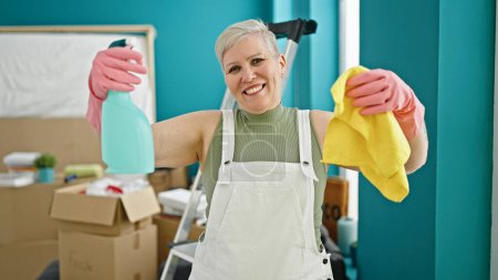 Photo for Middle age grey-haired woman smiling confident holding cloth and sprayer at new home - Royalty Free Image