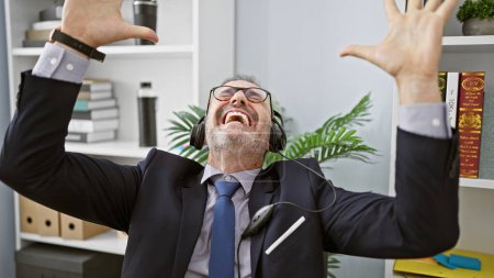 Photo for Confident middle age man with grey hair, a smiling business worker wearing headset, celebrating his win at the office - a winner in his professional indoor workplace - Royalty Free Image