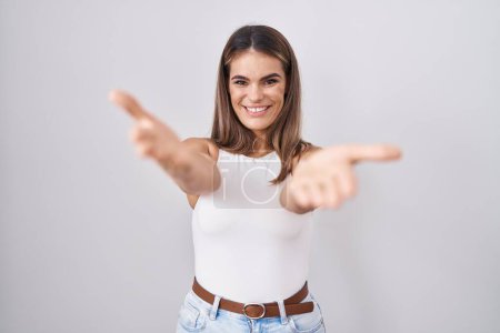Téléchargez les photos : Jeune femme hispanique debout sur fond blanc souriant joyeuse offrant des mains donnant assistance et acceptation. - en image libre de droit