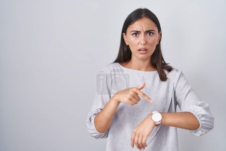 Téléchargez les photos : Young hispanic woman standing over white background in hurry pointing to watch time, impatience, upset and angry for deadline delay - en image libre de droit