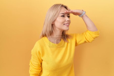 Téléchargez les photos : Jeune femme caucasienne portant un pull jaune très heureuse et souriante regardant loin avec la main au-dessus de la tête. concept de recherche. - en image libre de droit