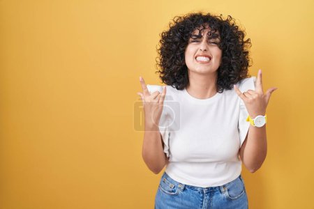 Photo for Young middle east woman standing over yellow background shouting with crazy expression doing rock symbol with hands up. music star. heavy concept. - Royalty Free Image