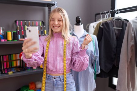 Téléchargez les photos : Jeune créatrice de couturière caucasienne sur appel vidéo avec smartphone criant fier, célébrant la victoire et le succès très excité avec bras levé - en image libre de droit