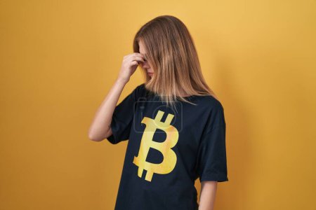 Photo for Blonde caucasian woman wearing bitcoin t shirt tired rubbing nose and eyes feeling fatigue and headache. stress and frustration concept. - Royalty Free Image