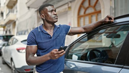 Photo for African american man using smartphone leaning on car at street - Royalty Free Image