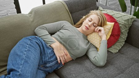 Photo for A young caucasian woman with short blonde hair sleeps peacefully on a sofa in a cozy indoor home setting. - Royalty Free Image
