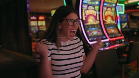 Foto de Mujer joven emocionada celebrando una victoria en las máquinas tragamonedas en un casino. - Imagen libre de derechos