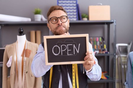 Photo for Middle age man with beard dressmaker designer holding open sign serious face thinking about question with hand on chin, thoughtful about confusing idea - Royalty Free Image