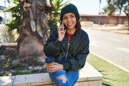 Téléchargez les photos : Jeune belle femme hispanique parlant sur smartphone boire du café au parc - en image libre de droit