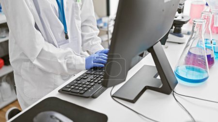 A woman scientist in a laboratory works diligently on a computer, amidst beakers and scientific equipment.