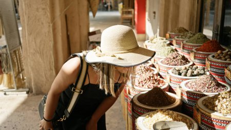 Téléchargez les photos : Une jeune femme explore un marché traditionnel à Dubai, examinant les épices et les herbes dans un souk arabe. - en image libre de droit