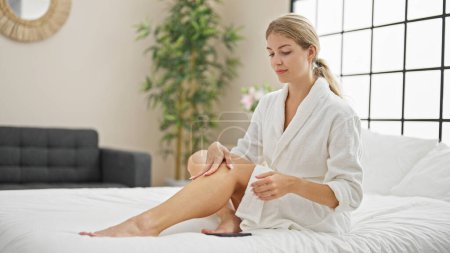 Photo for Young blonde woman wearing bathrobe massaging leg at bedroom - Royalty Free Image