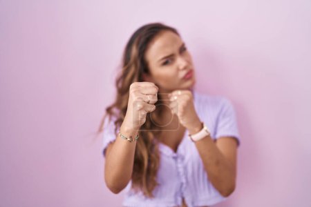 Téléchargez les photos : Jeune femme hispanique debout sur fond rose prêt à se battre avec geste de défense poing, visage en colère et bouleversé, peur du problème - en image libre de droit