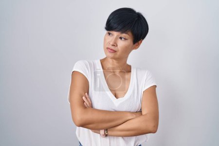 Téléchargez les photos : Jeune femme asiatique avec les cheveux courts debout sur fond isolé regardant sur le côté avec les bras croisés convaincu et confiant - en image libre de droit