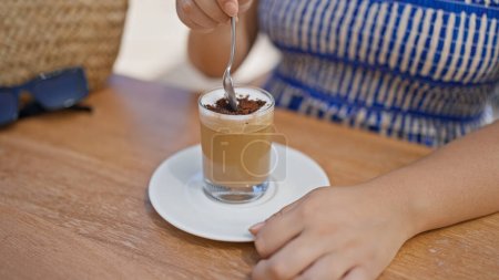 Téléchargez les photos : Jeune femme hispanique agitant café assis sur la table à la terrasse ensoleillée du restaurant - en image libre de droit
