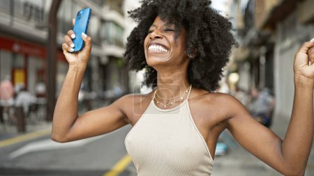 Foto de Mujer afroamericana usando smartphone celebrando en la calle - Imagen libre de derechos