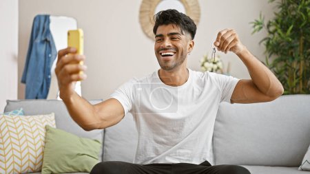 Handsome hispanic man smiling while taking a selfie at home, portraying a casual and joyful indoor lifestyle