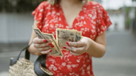 Téléchargez les photos : Jeune femme prise dans l'agitation de la ville de Tokyo, les mains occupées à compter les piles de billets en yen au milieu de la belle architecture de l'économie urbaine moderne du Japon - en image libre de droit