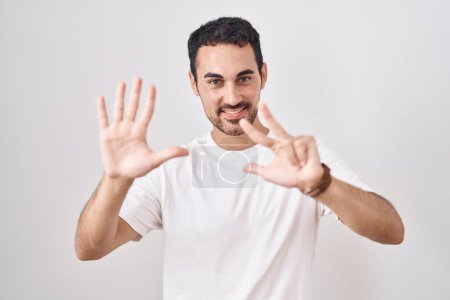 Foto de Hombre hispano guapo de pie sobre fondo blanco mostrando y señalando hacia arriba con los dedos número ocho mientras sonríe confiado y feliz. - Imagen libre de derechos