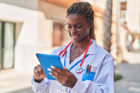 Téléchargez les photos : Afro-américaine femme médecin souriant confiant en utilisant touchpad à la rue - en image libre de droit