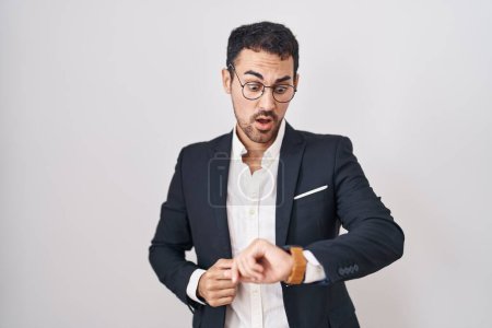 Téléchargez les photos : Beau homme d'affaires hispanique debout sur fond blanc regardant le temps de la montre inquiet, peur de se faire tard - en image libre de droit