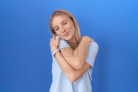 Téléchargez les photos : Jeune femme caucasienne portant un t-shirt bleu décontracté s'embrassant heureux et positif, souriant confiant. amour de soi et soins de soi - en image libre de droit