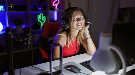 Photo for A smiling young woman enjoys gaming with headphones in a colorful neon-lit room at night. - Royalty Free Image