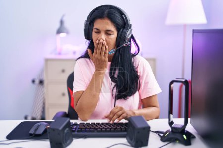 Foto de Mujer hispana madura jugando videojuegos en casa aburrida bostezando cansada cubriendo la boca con la mano. inquietud y somnolencia. - Imagen libre de derechos