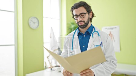 Photo for Young hispanic man doctor reading medical report at the clinic - Royalty Free Image