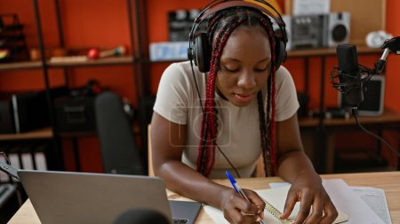 Téléchargez les photos : Au cœur d'un studio de radio, une belle musicienne afro-américaine s'assoit à la table, tresses oscillantes, composant habilement un chef-d'œuvre musical avec une touche de magie noire - en image libre de droit