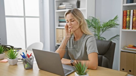 Foto de Una joven profesional que se siente estresada en un escritorio de oficina moderno con computadora portátil - Imagen libre de derechos