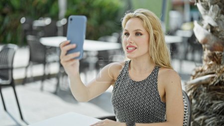 Téléchargez les photos : Jeune femme blonde souriante confiante ayant appel vidéo à la terrasse du café - en image libre de droit