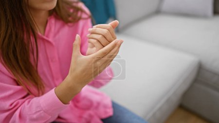 Foto de La mujer hispana que sufre dolor de manos, sentada en el sofá, dolor de muñeca en casa subraya el problema, el fondo de la lesión interior revela el brazo herido - Imagen libre de derechos